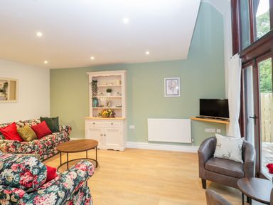 A living room with floral sofas a wooden cabinet a round coffee table a small television and a leather armchair at The Forge in Shipham