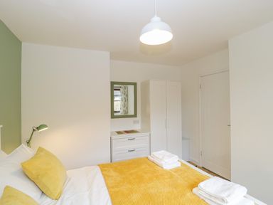 A bedroom with a bed with yellow pillows and blanket a white dresser with mirror and a white wardrobe at The Forge in Shipham