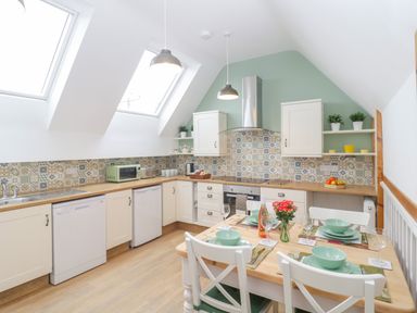 A kitchen with tiled backsplash white cabinets wooden countertops dining table set with green dishes and flowers at The Forge in Shipham