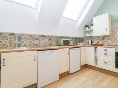 A kitchen with white cabinets a dishwasher a small refrigerator countertop appliances and skylight windows at The Forge in Shipham