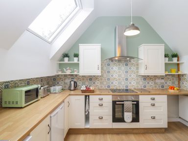 A kitchen with a skylight window white cabinets wooden countertops patterned tile backsplash and appliances at The Forge in Shipham
