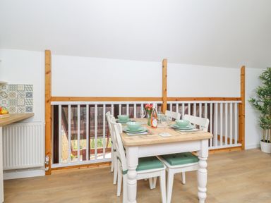 A dining table set with plates bowls and glasses in a room with wooden flooring and white walls at The Forge in Shipham
