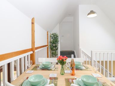 A dining area with a wooden table set with green dishes wine glasses and a bottle with a plant and white railing at The Forge in Shipham
