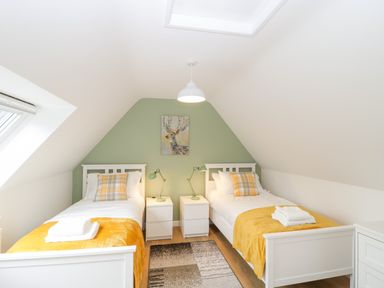 A bedroom with two single beds white bedding yellow throws and plaid pillows at The Forge in Shipham