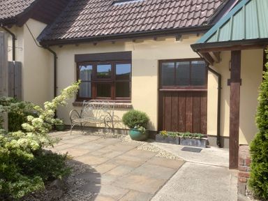 A paved courtyard with a metal bench plants and a building with tiled roof and windows at The Forge in Shipham