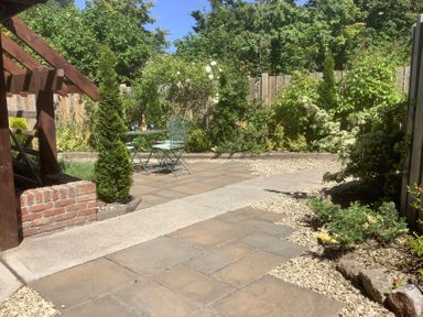 A garden patio with a small metal table and two chairs surrounded by plants and a wooden fence at The Forge in Shipham