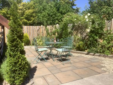 An outdoor patio area with a metal table and four chairs surrounded by plants and a wooden fence at The Forge in Shipham