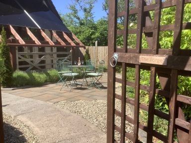 An outdoor patio with a metal table and four chairs with cushions beside a wooden gate at The Forge in Shipham