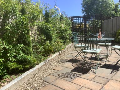 A garden patio with metal table and chairs with cushions and a bottle with glasses on the table at The Forge in Shipham