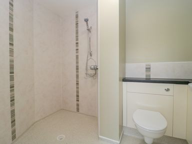 A bathroom with a shower area and a built in toilet with storage cabinets at Mendip Cottage in Shipham