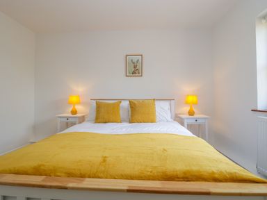 A bedroom with a bed with yellow pillows and blanket two bedside tables with lamps and a framed picture above the bed at Mendip Cottage in Shipham