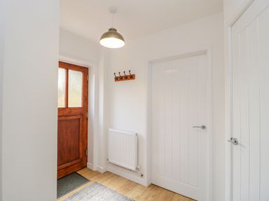 An entryway with a wooden door a white radiator a coat rack and two white doors at Mendip Cottage in Shipham