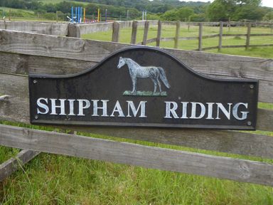 A wooden fence with a sign that reads Shipham Riding and an illustration of a horse at Shipham Riding in Shipham