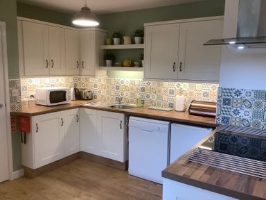 A kitchen with white cabinets patterned backsplash wooden countertops and appliances at Mendip Cottage in Shipham