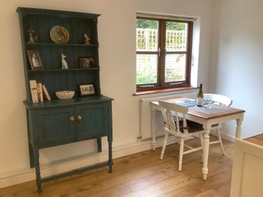 A dining area with a small wooden table set for two and a blue cabinet with shelves displaying decorative items at Mendip Cottage in Shipham