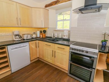 A kitchen with wooden cabinets a dishwasher stove toaster coffee maker and sink at Tilberthwaite Farm Cottage in Coniston