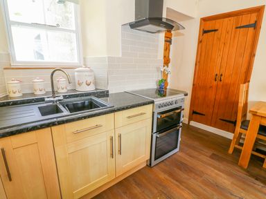 A kitchen with black countertop double sink stove wooden cabinets wooden door and dining table at Tilberthwaite Farm Cottage in Coniston