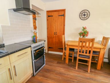A kitchen with wooden cabinets a stainless steel oven wooden dining table with chairs and a wall clock at Tilberthwaite Farm Cottage in Coniston