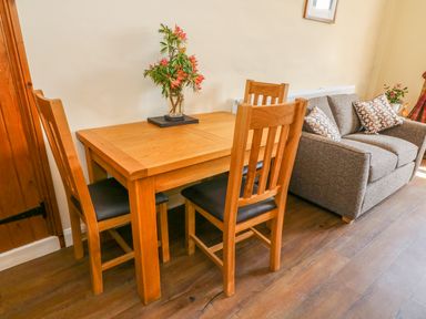 A dining area with a wooden table and chairs next to a sofa with patterned cushions at Tilberthwaite Farm Cottage in Coniston