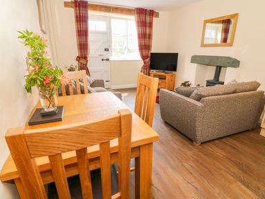 A living room with a wooden dining table and chairs a television on a cabinet and a wood burning stove at Tilberthwaite Farm Cottage in Coniston