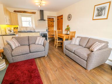 A living room with two sofas a wooden dining table a kitchen area and wooden doors at Tilberthwaite Farm Cottage in Coniston