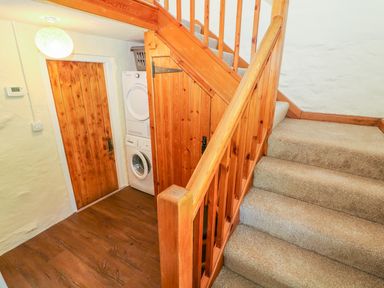 A carpeted staircase with wooden handrails next to a laundry area with stacked washer and dryer at Tilberthwaite Farm Cottage in Coniston