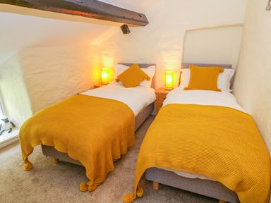A bedroom with two single beds yellow blankets and pillows a wooden beam and bedside tables at Tilberthwaite Farm Cottage Coniston