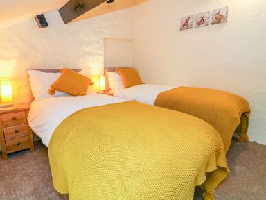 A bedroom with two single beds yellow blankets and pillows wooden nightstand with lamps and bunny paintings on the wall at Tilberthwaite Farm Cottage in Coniston