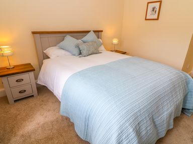A bedroom with a double bed with blue quilt and pillows two bedside tables with lamps and a framed picture on the wall at Tilberthwaite Farm Cottage in Coniston
