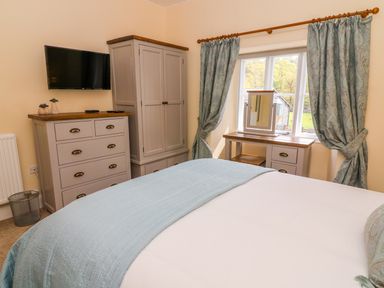 A bedroom with a bed a chest of drawers a wardrobe a dressing table with a mirror and curtains on a window at Tilberthwaite Farm Cottage Coniston