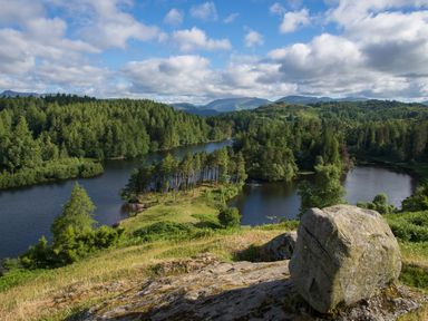 A view of a river surrounded by trees hills and rocks under a cloudy sky at Tilberthwaite Farm Cottage in Coniston