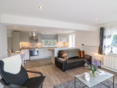 An open plan living room and kitchen with a black leather sofa and a dining table at Cuckoo Cottage in Bridport