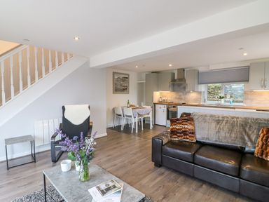 An open plan living room and kitchen with a black leather sofa and dining table at Cuckoo Cottage in Bridport