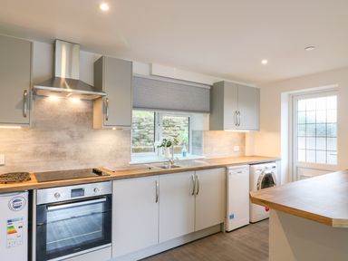 A kitchen with an oven stove extractor fan sink dishwasher washing machine and window at Cuckoo Cottage in Bridport