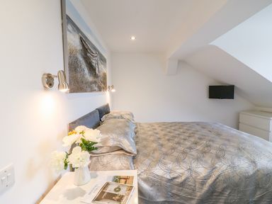 A bedroom with a bed covered with patterned bedding a bedside table with flowers a dresser and a wall-mounted TV at Cuckoo Cottage in Bridport