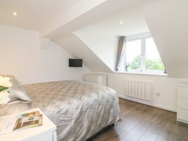 A bedroom with a bed bedside table window mounted tv and white furniture at Cuckoo Cottage in Bridport
