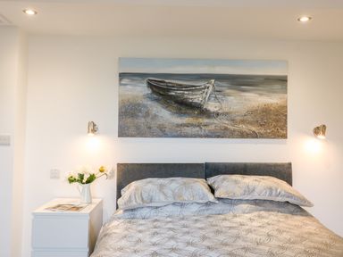 A bedroom with a bed patterned bedding a nightstand with flowers and a wall painting of a boat at Cuckoo Cottage in Bridport