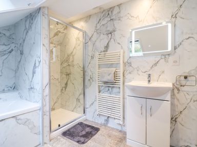 A bathroom with a shower enclosure bathtub sink with cabinet towel rail and illuminated mirror at Cuckoo Cottage in Bridport