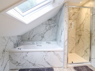 A bathroom with a bathtub under a skylight and a shower with marble walls at Cuckoo Cottage in Bridport