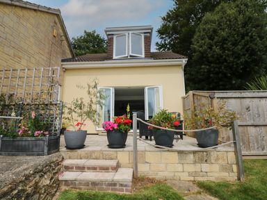 A patio with potted plants and outdoor furniture beside a yellow house with open white doors at Cuckoo Cottage in Bridport