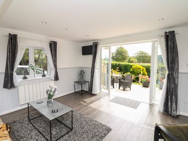 A living room with a coffee table and flowers by a window and sliding doors opening to a garden at Cuckoo Cottage in Bridport