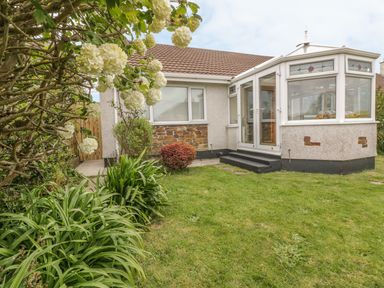 A house with a conservatory and garden with plants and white flowers at Dune Haven in Goonhavern near Perranporth