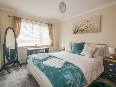 A bedroom with a bed blankets pillows bedside tables lamps a standing mirror and a window at Dune Haven in Goonhavern near Perranporth