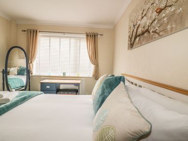A bedroom with a bed with pillows a blue desk a standing mirror and a window with curtains at Dune Haven in Goonhavern near Perranporth