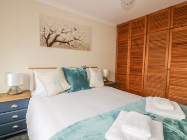 A bedroom with a bed with pillows and folded towels on a blanket and wooden wardrobe at Dune Haven in Goonhavern near Perranporth
