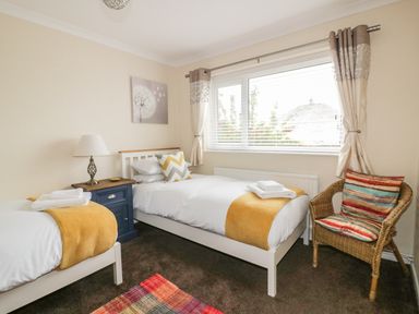 A bedroom with two single beds a blue nightstand a lamp striped cushions and a window at Dune Haven in Goonhavern near Perranporth