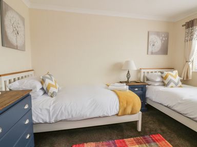 A bedroom with two single beds a blue chest of drawers a bedside table with a lamp and a window at Dune Haven in Goonhavern near Perranporth