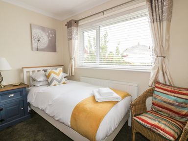A bedroom with a bed blue nightstand and a wicker chair with colorful cushions at Dune Haven in Goonhavern near Perranporth
