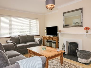 A living room with grey sofas a wooden coffee table a fireplace and a television at Dune Haven in Goonhavern near Perranporth