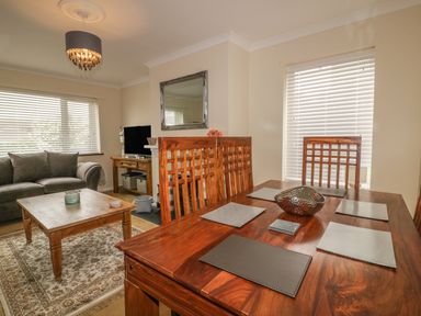 A dining table with placemats and a bowl next to a living area with a sofa and coffee table at Dune Haven in Goonhavern near Perranporth